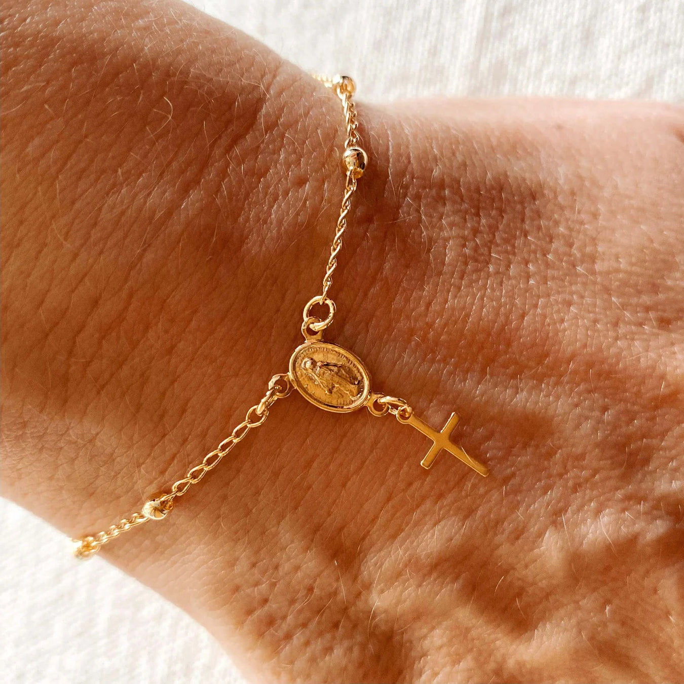 Gold bracelet with a cross and circular charm on a wrist against a white background