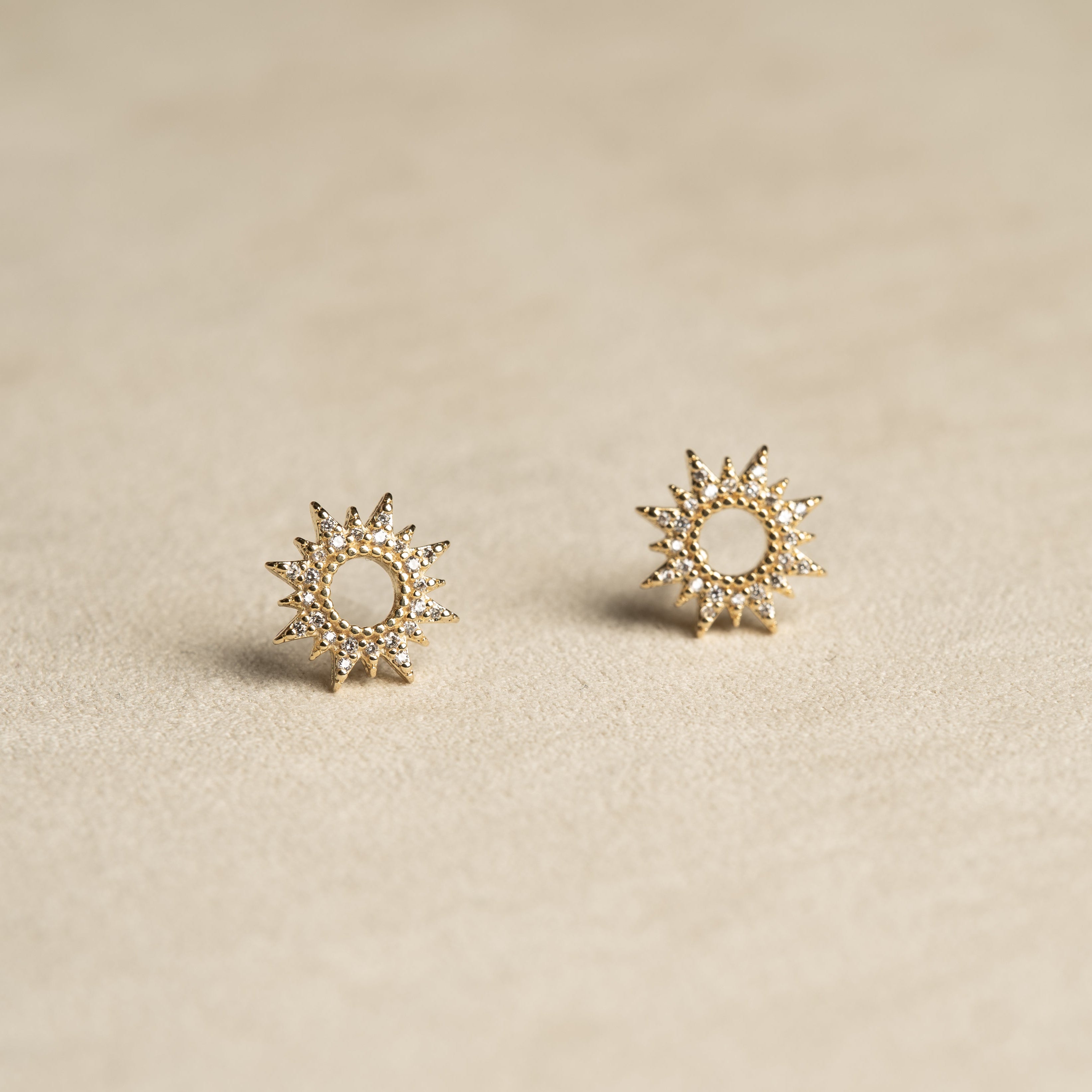 Pair of gold sun-shaped earrings on a beige background